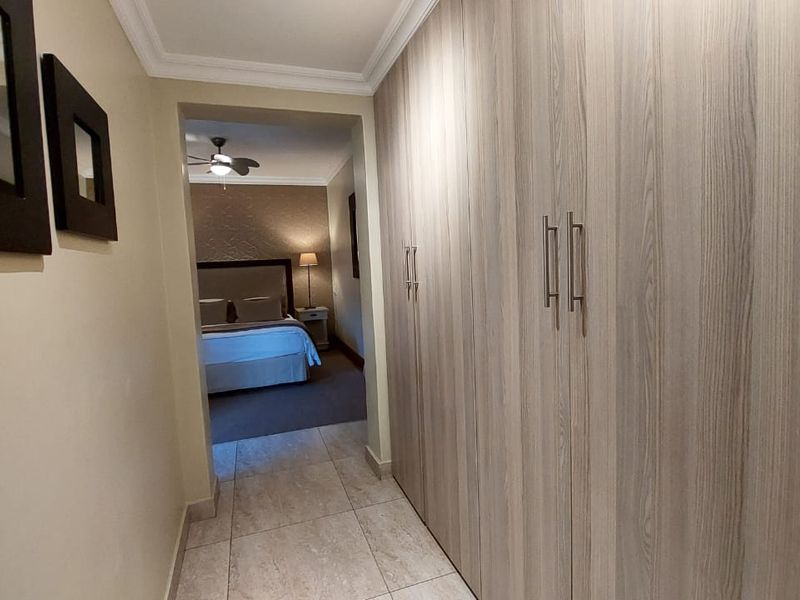 A well-maintained hallway featuring extensive built-in cabinetry with wood-grain finish, tiled flooring, and coving, leading into a bedroom.