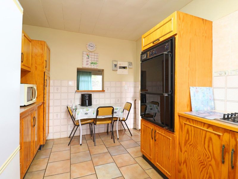 A dated kitchen featuring wooden cabinetry, tiled backsplash, built-in oven, gas hob, and a convenient serving hatch to the adjacent room.