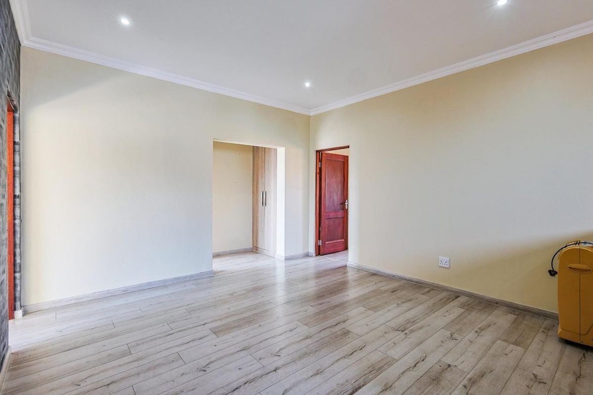 A bright, empty bedroom featuring light wood-look laminate flooring, recessed ceiling lighting, and an adjoining walk-in closet area with built-in cabinetry.