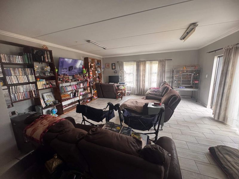 Spacious living room featuring tiled flooring and built-in shelving units, offering a functional layout with natural light from large windows.