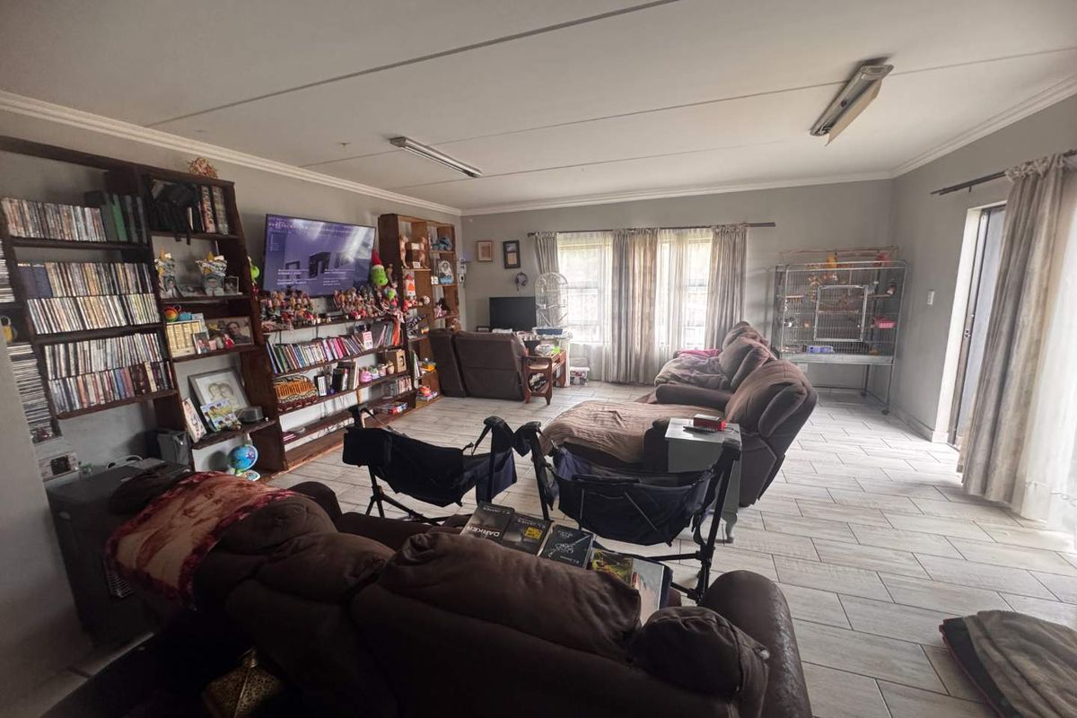 Spacious living room featuring tiled flooring and built-in shelving units, offering a functional layout with natural light from large windows.