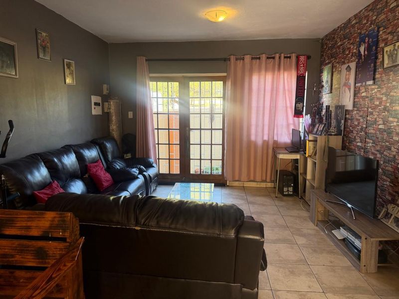 A living room featuring tiled flooring, a brick-effect feature wall, and french doors providing access to the exterior.