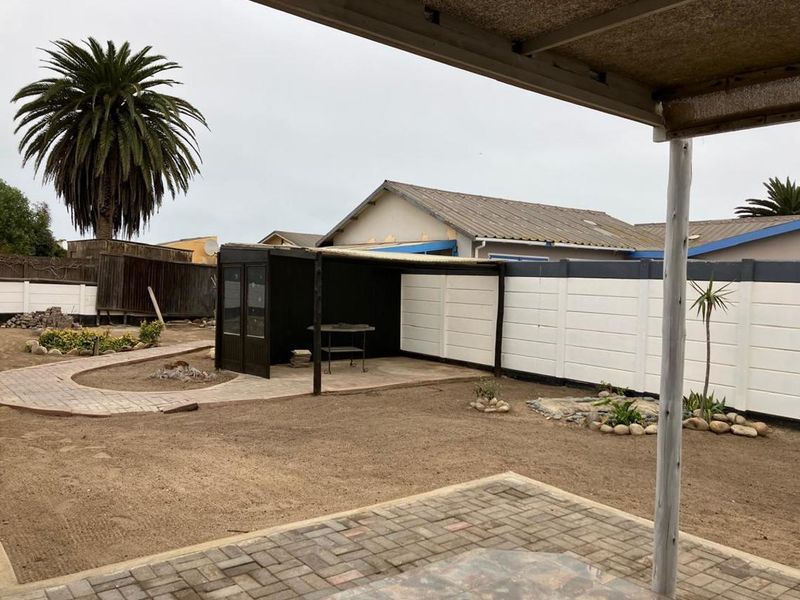 Rear garden area featuring a paved patio, a covered outdoor structure, and a precast concrete boundary wall with potential for landscaping improvements.