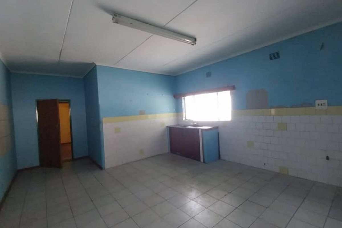 A spacious, empty kitchen area featuring tiled flooring, basic cabinetry, and a window, offering a blank canvas for renovation and modernization.