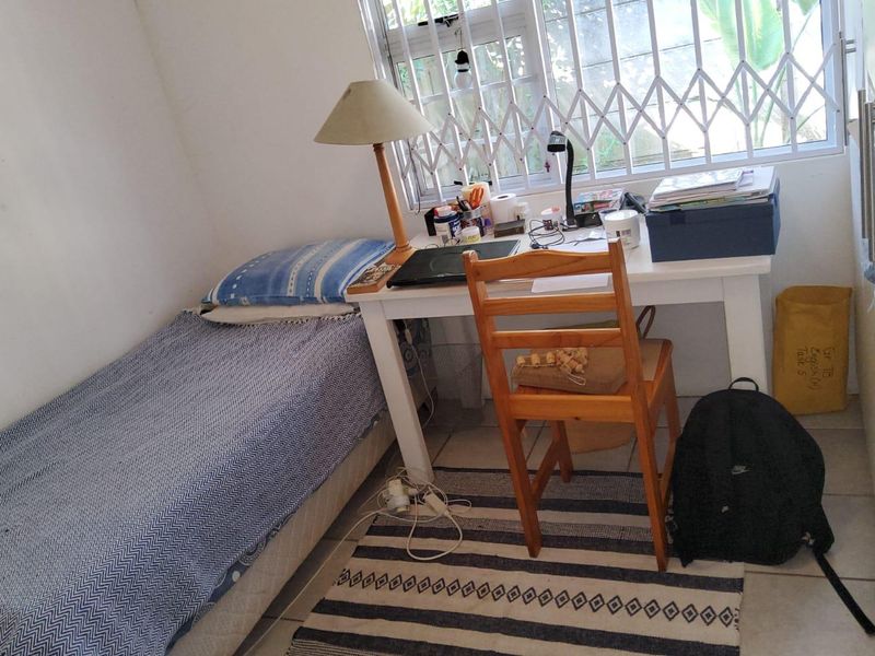 A compact bedroom featuring tiled flooring, a built-in cupboard, and a window fitted with a security gate.