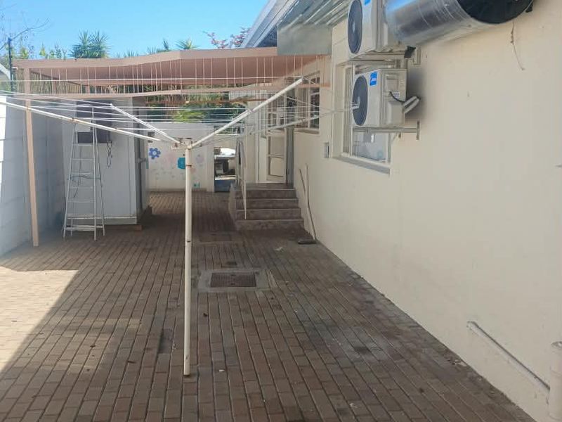 Rear exterior courtyard featuring paved flooring, external geyser, air conditioning units, and a covered patio area with concrete steps leading to the house.