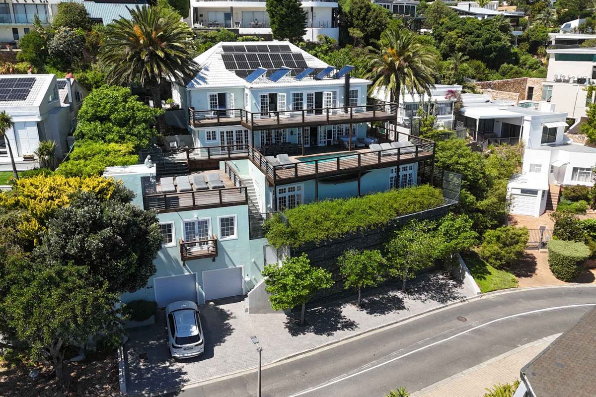 Aerial view of a multi-level residential property featuring extensive timber decking, a swimming pool, solar panels, and a double garage.