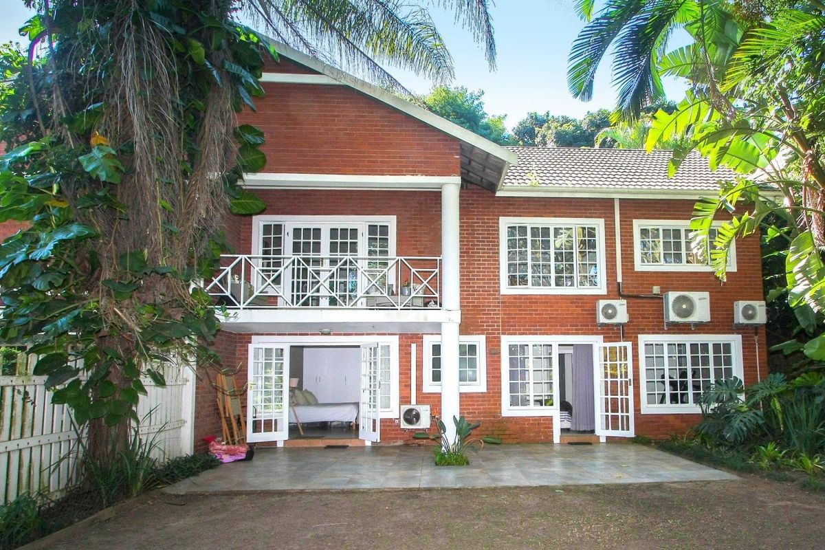 Rear view of a two-story brick house featuring a ground-level tiled patio, upper balcony, and multiple access points through french doors.