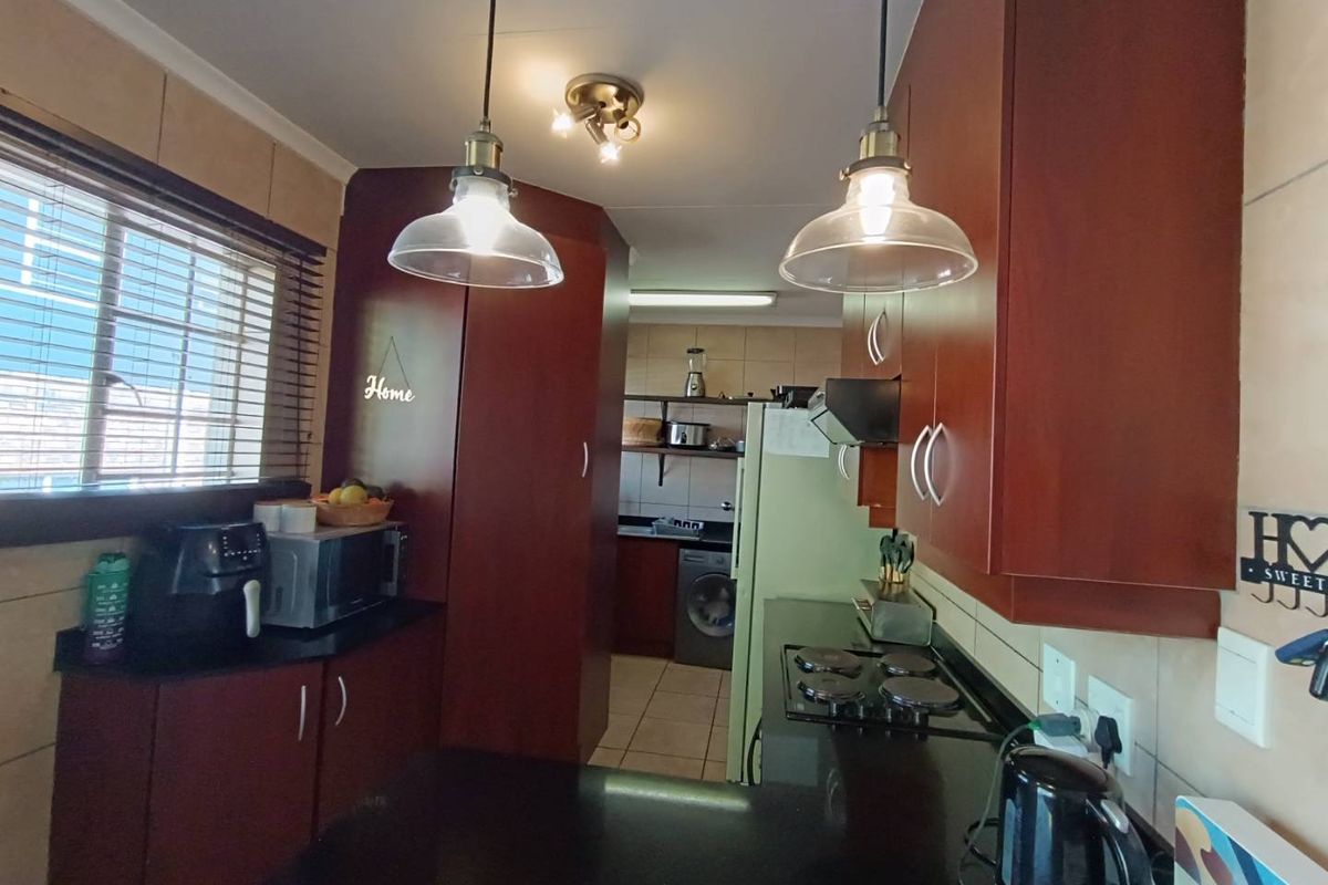 A functional kitchen featuring dark wood cabinetry, granite countertops, a built-in electric hob, and an adjoining scullery area with laundry connections.