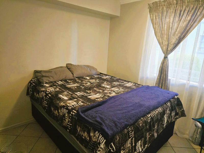 A standard bedroom featuring tiled flooring and a window with installed curtain rails, providing a functional and neutral living space.