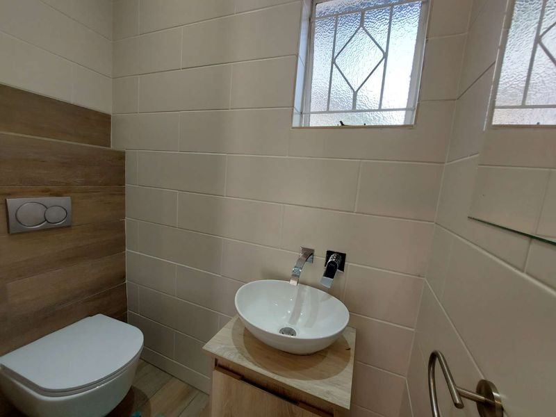 Modern guest bathroom featuring a wall-mounted toilet, vessel sink with wall-mounted faucet, and contemporary tiled finishes.