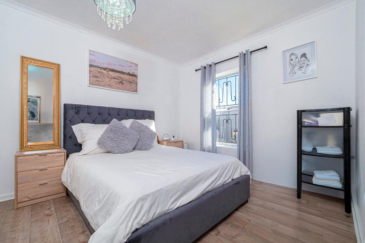 A well-lit bedroom featuring wood-look laminate flooring, a window with security bars, and a modern light fixture.