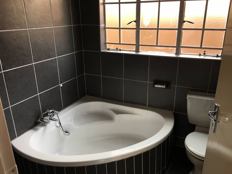 A bathroom featuring a corner bathtub, toilet, and dark tiled walls with a window providing natural light.