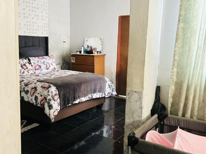 A bedroom featuring dark tiled flooring and a panelled ceiling, showing signs of wear on the wall finishes.