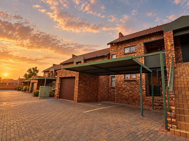 Exterior view of a face brick apartment complex featuring paved parking areas, carports, and private garage access at sunset.