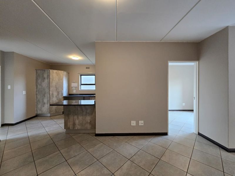 An open-plan living and kitchen area featuring neutral wall tones, tiled flooring, and modern built-in cabinetry with a functional kitchen island.