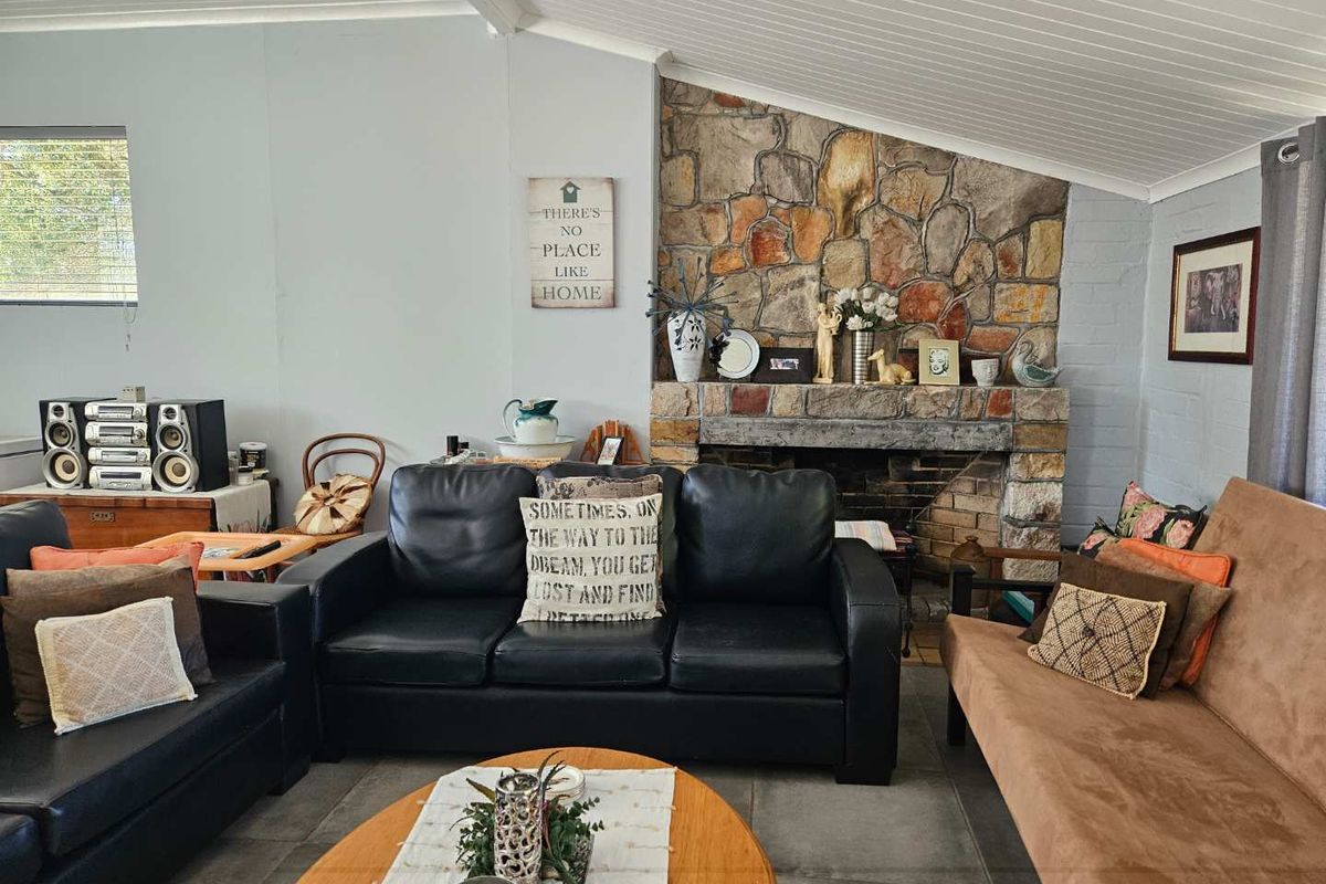 A cozy living room featuring a prominent natural stone fireplace, vaulted timber-paneled ceiling, and tiled flooring.