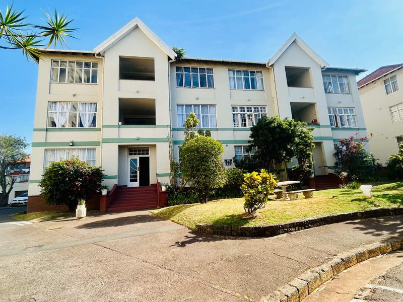 Front elevation of a multi-story apartment building featuring a landscaped garden, concrete entrance steps, and classic casement window design.