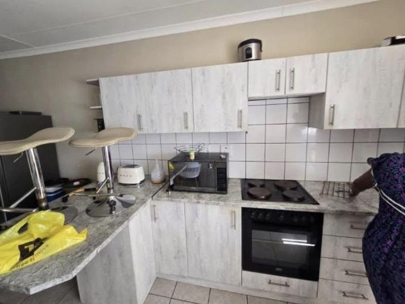 A functional kitchen featuring light wood-grain cabinetry, tiled backsplash, and integrated appliances including an electric hob and oven.
