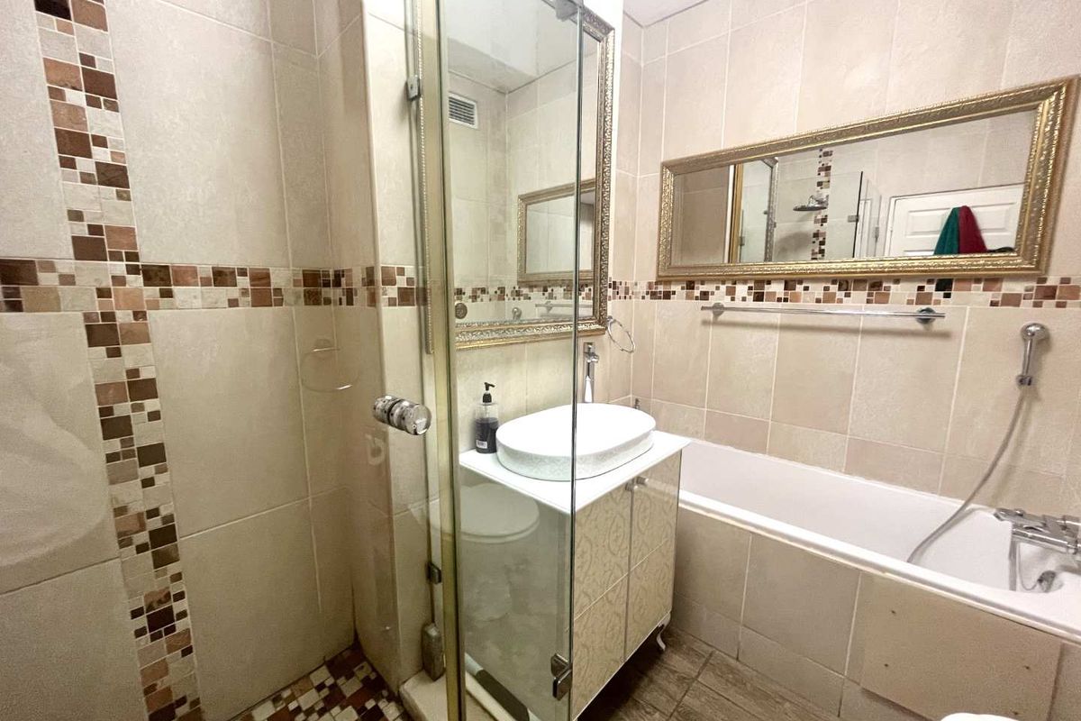 A compact bathroom featuring a glass-enclosed shower, a built-in bathtub, a vanity with a vessel sink, and decorative mosaic tile accents.