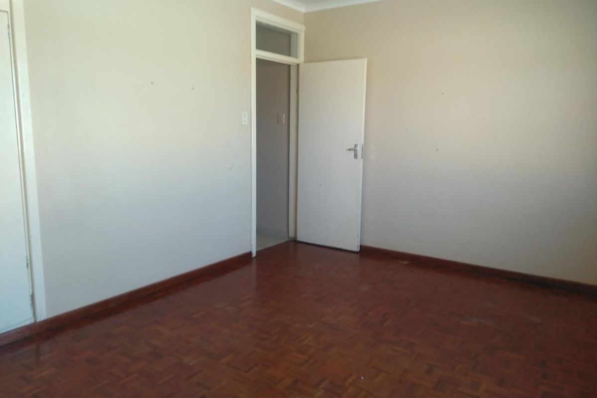 A vacant bedroom featuring original parquet flooring, neutral wall finishes, and a built-in cupboard.