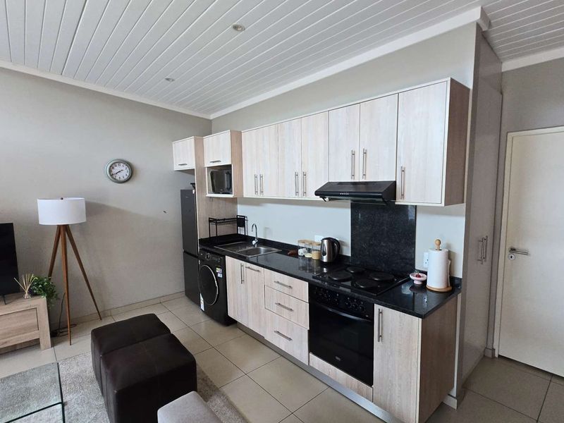 Modern open-plan kitchen featuring light wood cabinetry, granite countertops, integrated appliances, and tiled flooring, seamlessly connected to the living area.