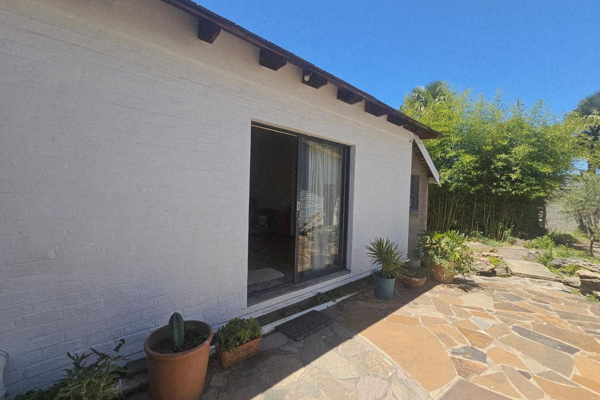 A rear exterior view featuring a white painted brick wall, sliding glass door access, and a natural stone paved patio area.