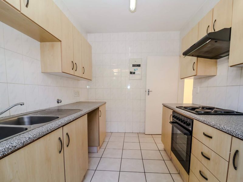 A functional galley-style kitchen featuring light wood-look cabinetry, granite-effect countertops, built-in oven, hob, and extractor fan with tiled finishes throughout.