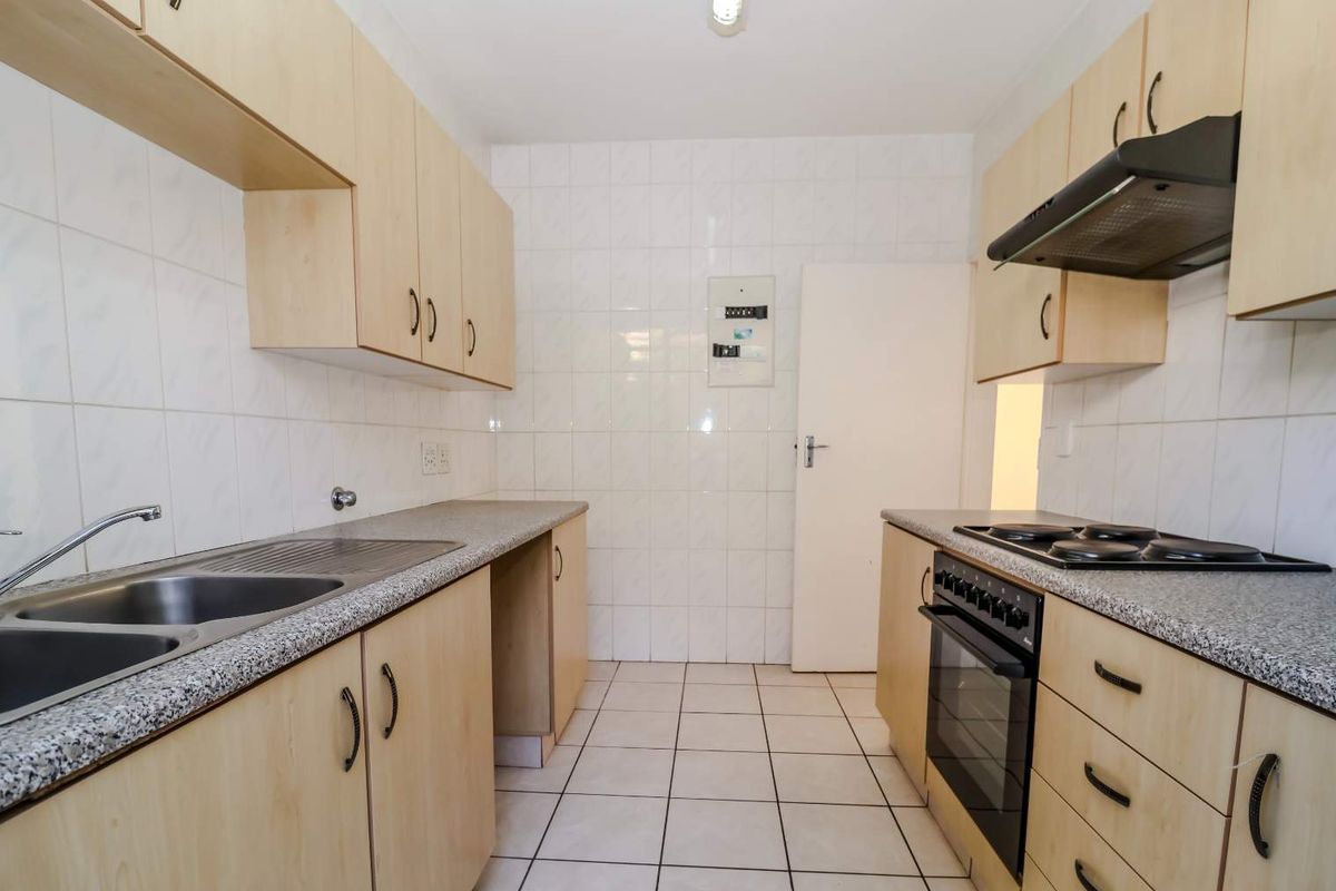 A functional galley-style kitchen featuring light wood-look cabinetry, granite-effect countertops, built-in oven, hob, and extractor fan with tiled finishes throughout.