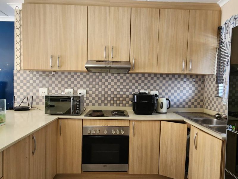 A functional kitchen featuring light wood-grain cabinetry, a tiled backsplash, built-in oven with electric hob, and a double bowl sink.