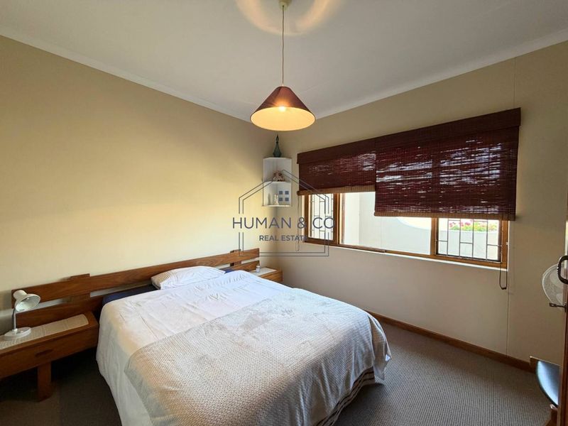 A functional bedroom featuring a built-in wooden headboard with integrated bedside tables, carpeted flooring, and window security bars.