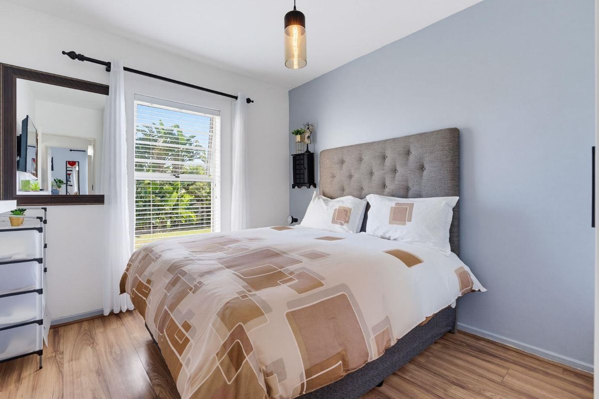 A well-maintained bedroom featuring laminate flooring, a feature wall, and a window with fitted blinds, providing a bright and comfortable living space.