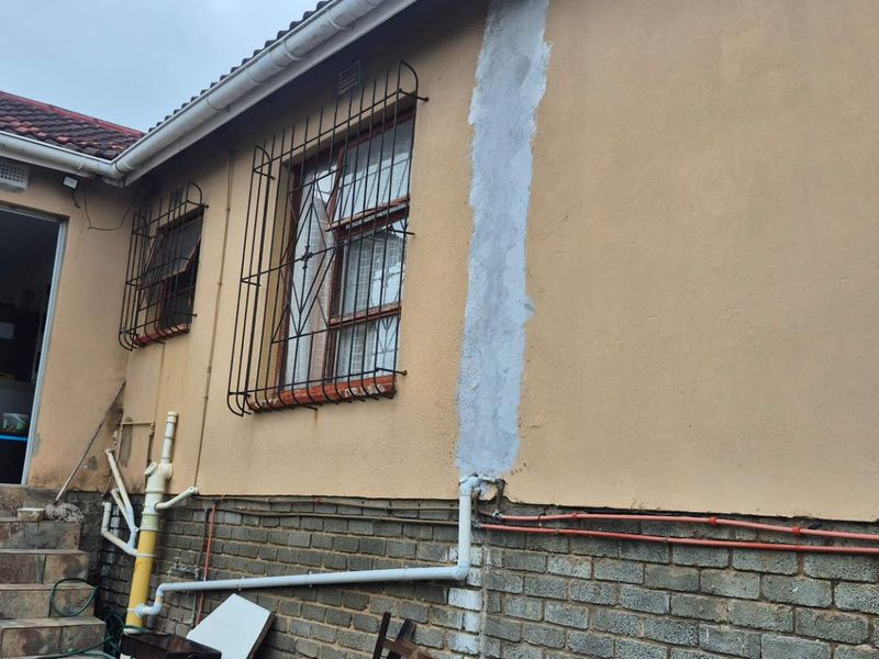Rear exterior view of the property showing tiled steps, security bars on windows, and visible exterior plumbing and masonry work.