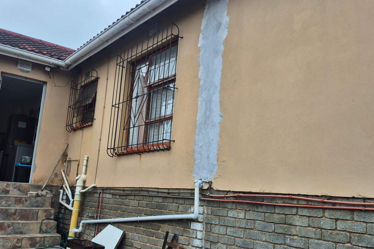 Rear exterior view of the property showing tiled steps, security bars on windows, and visible exterior plumbing and masonry work.
