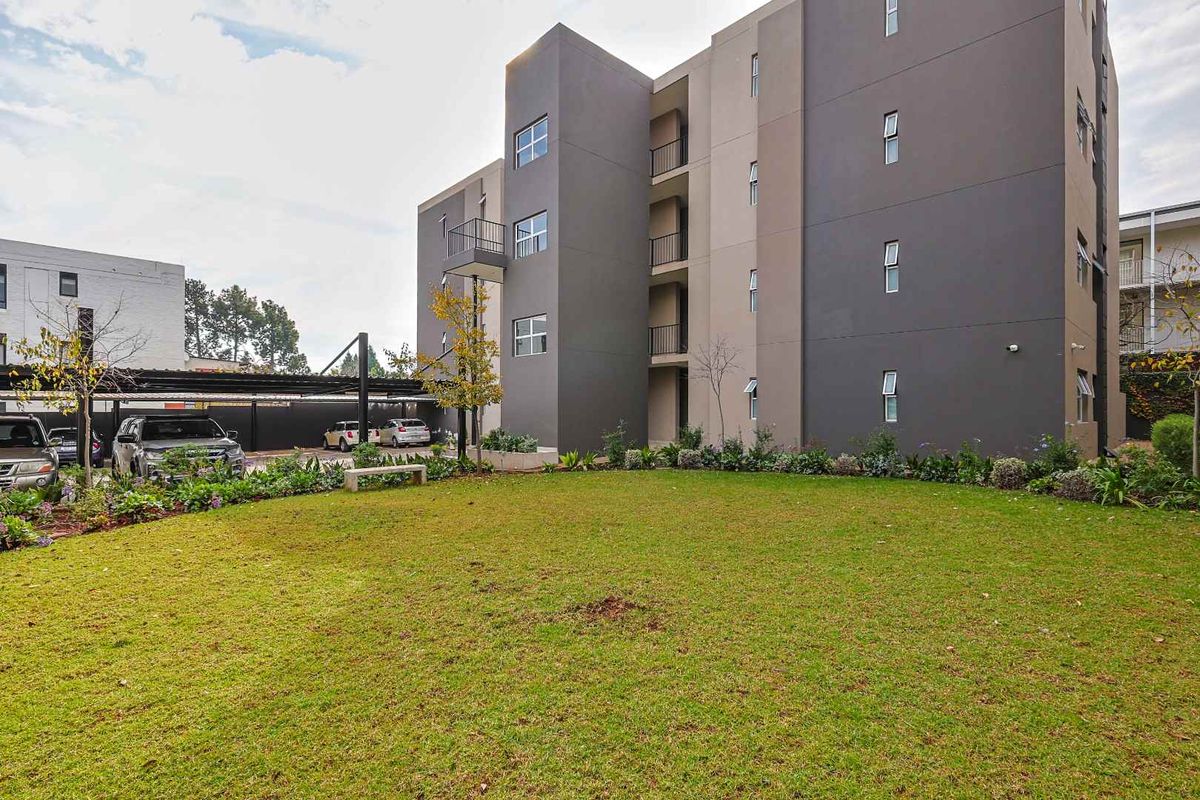 A view of the apartment building exterior featuring a well-maintained lawn, landscaped garden areas, and covered parking facilities.