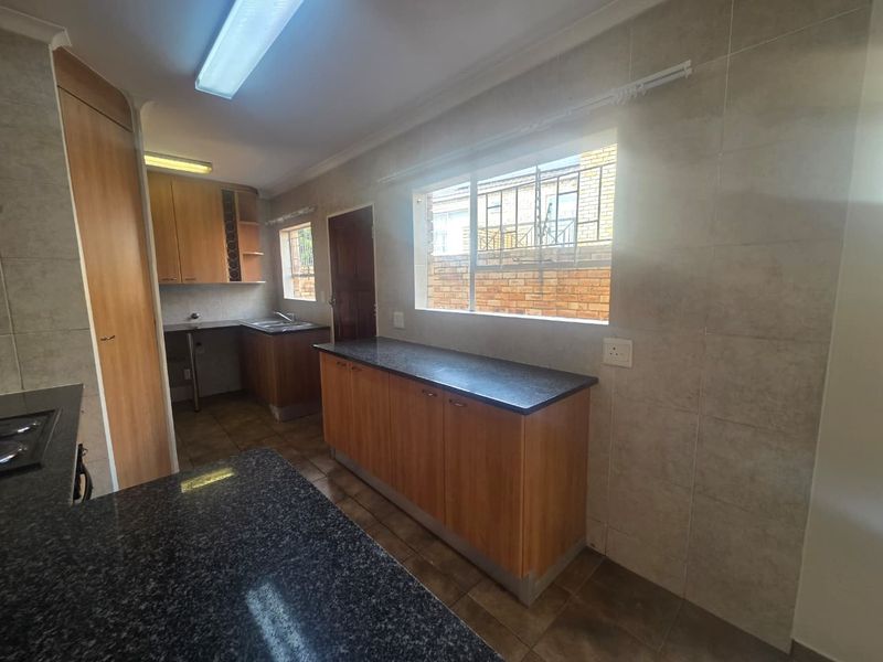 A functional kitchen featuring granite countertops, ample wooden cabinetry, tiled walls, and tiled flooring, offering a clean and practical workspace.