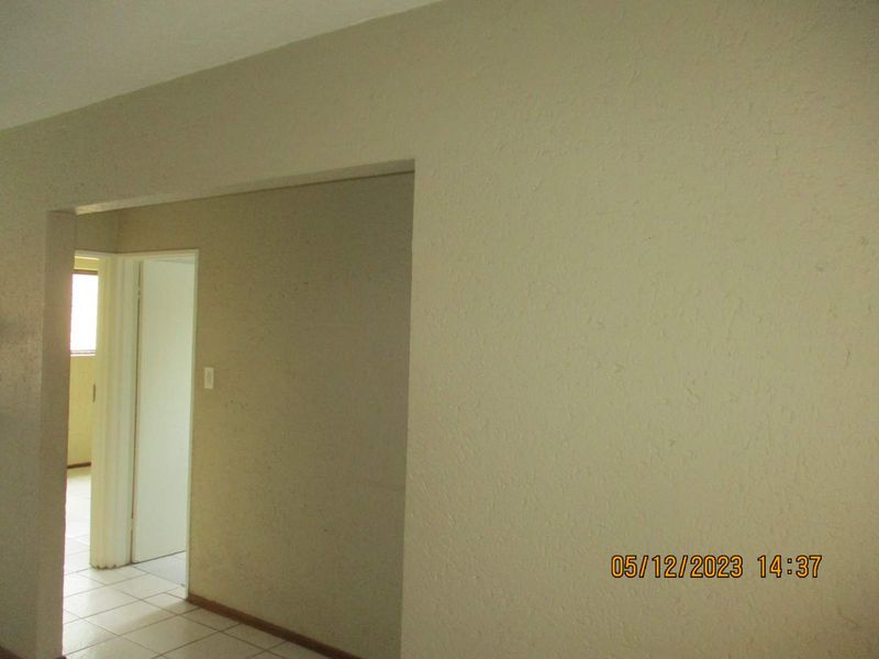 A view of an empty hallway featuring textured walls and tiled flooring, leading into an adjacent room.