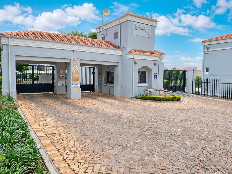 The secure entrance gate to Northcliff Terrace, featuring a cobblestone driveway, automated security gates, and well-maintained building facade.