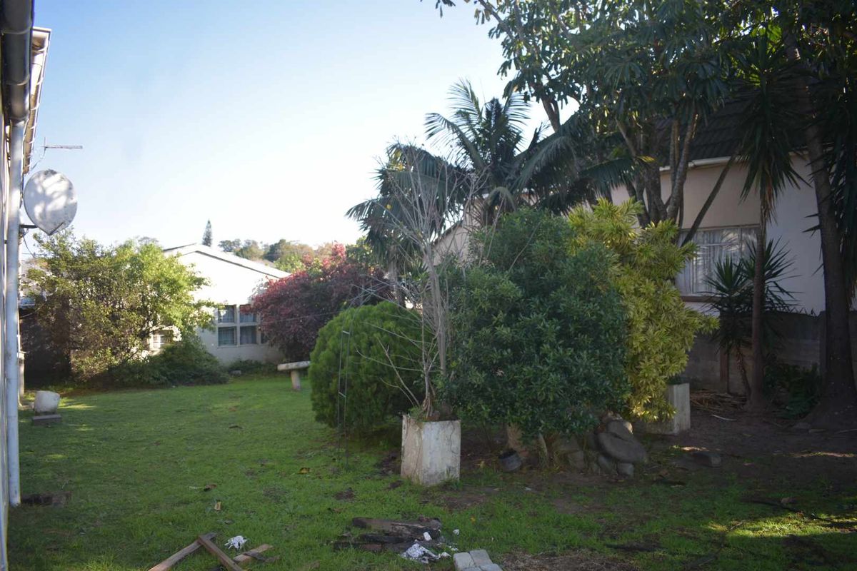 A view of the rear garden area featuring established trees, lawn space, and a satellite dish mounted on the building exterior.