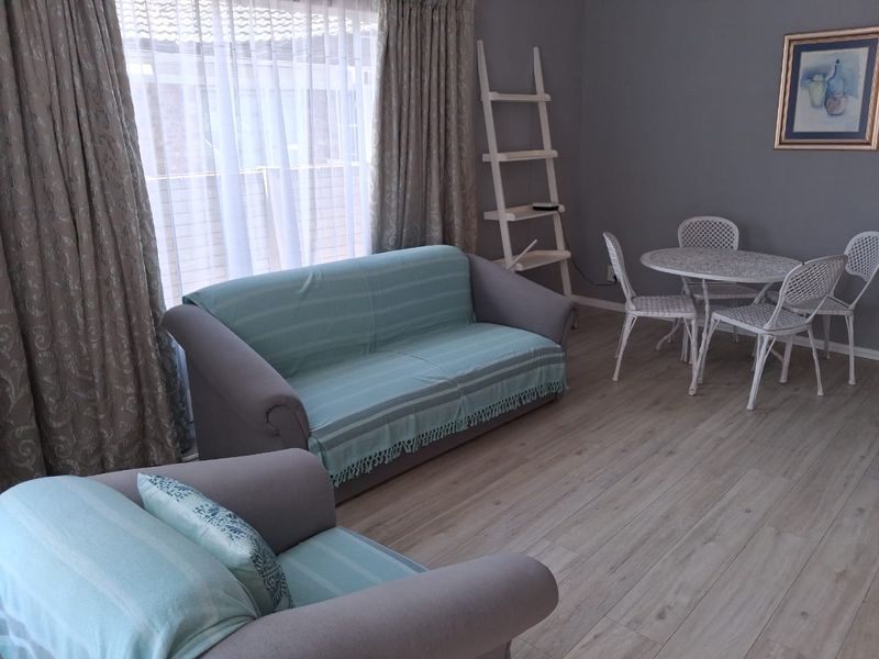 A well-maintained living room featuring light-toned laminate flooring and large windows with floor-to-ceiling curtains, providing a bright and neutral living space.