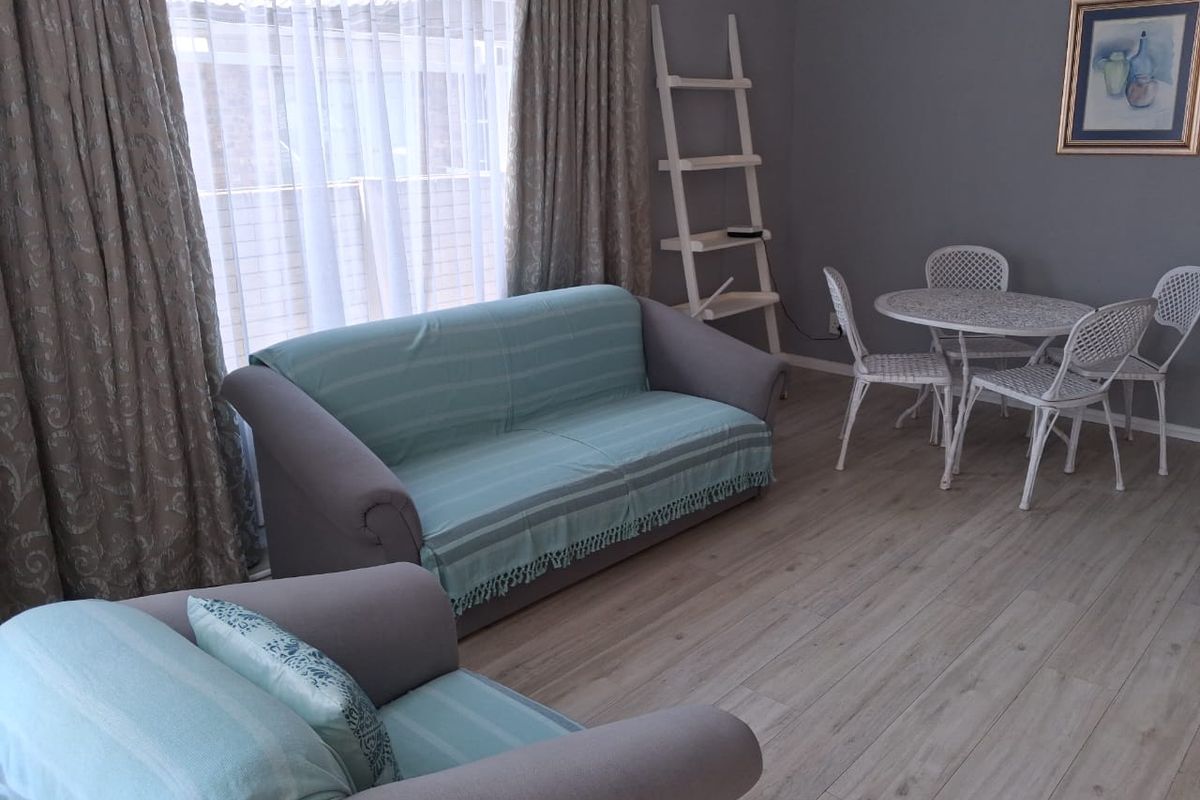 A well-maintained living room featuring light-toned laminate flooring and large windows with floor-to-ceiling curtains, providing a bright and neutral living space.