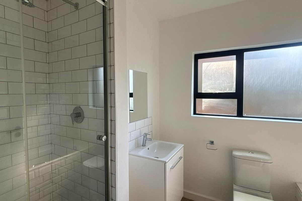 A modern bathroom featuring a glass-enclosed shower with white subway tiling, a vanity basin, and a toilet.