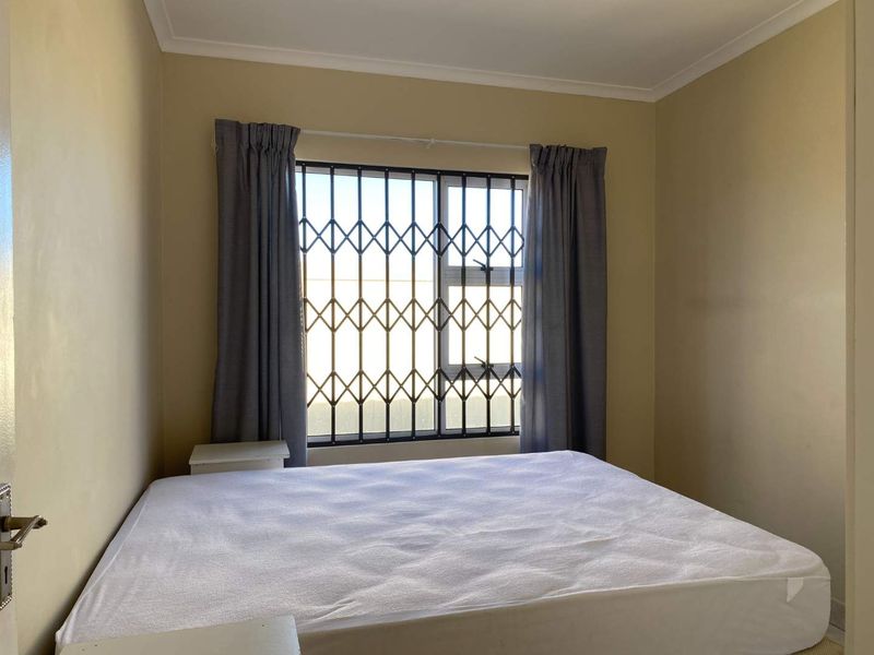 A standard bedroom featuring a window with a security gate and neutral wall finishes.