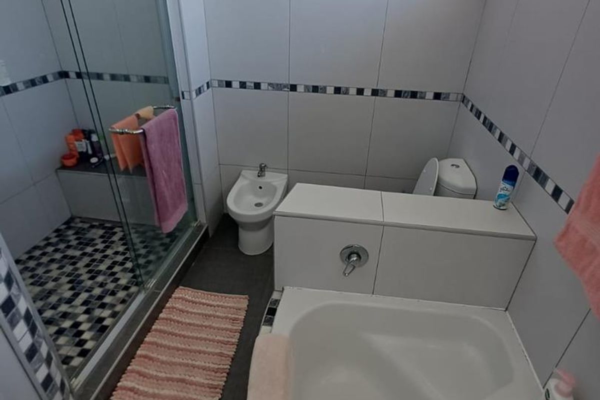 A functional bathroom featuring a glass-enclosed shower, a built-in bathtub, a bidet, and a toilet with neutral wall tiling and decorative mosaic accents.