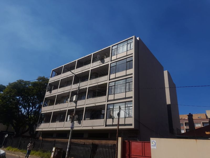 A multi-story apartment building featuring a structured facade with balconies and secure perimeter fencing.