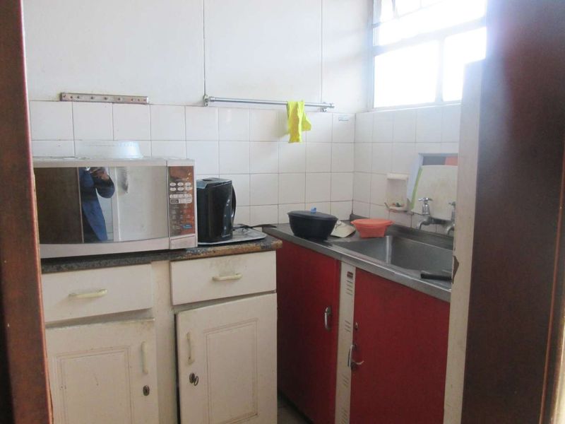 A compact kitchen featuring a stainless steel sink, tiled backsplash, and dated built-in cabinetry in need of modernization.