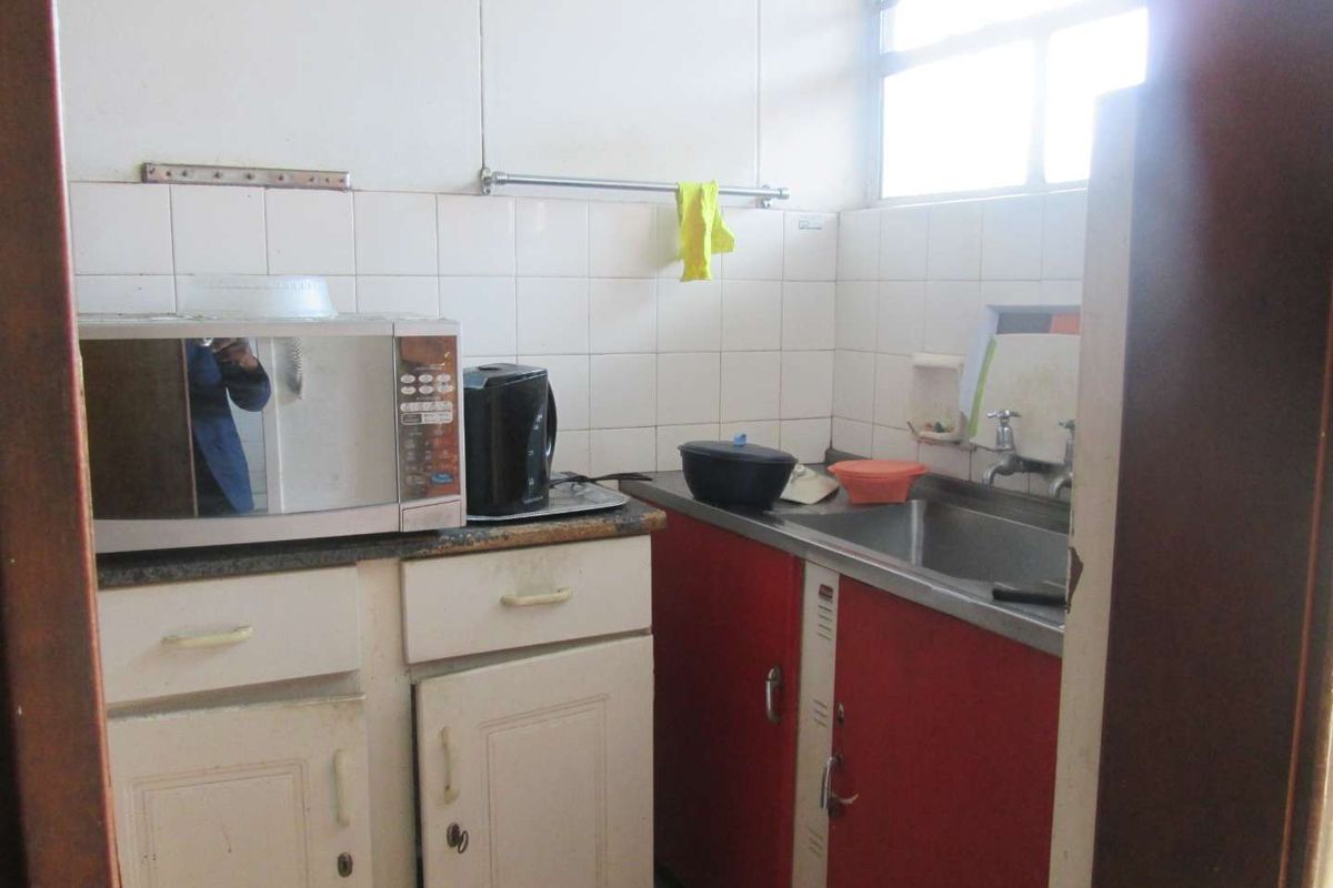 A compact kitchen featuring a stainless steel sink, tiled backsplash, and dated built-in cabinetry in need of modernization.