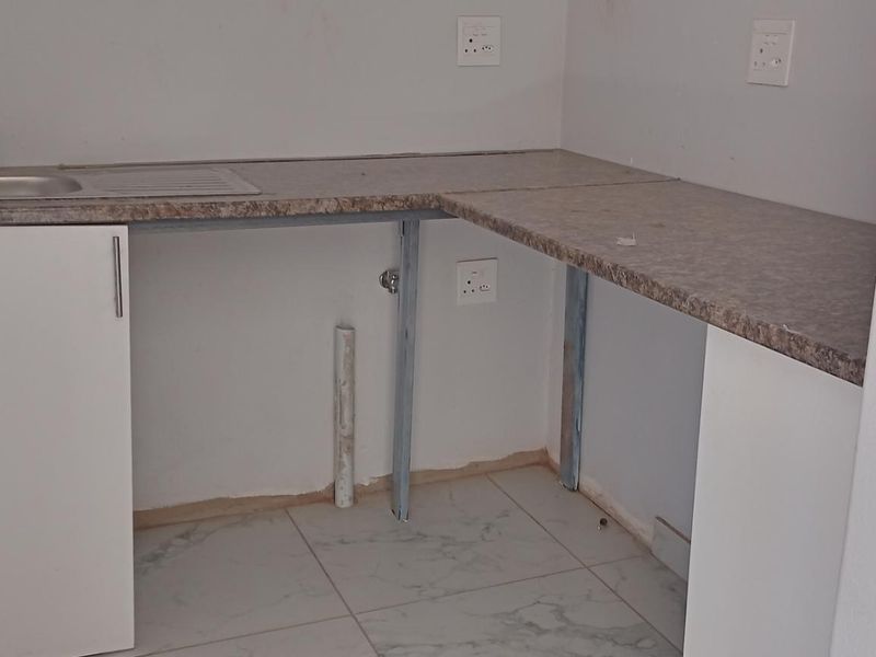 A compact kitchen area featuring a laminate countertop, stainless steel sink, and tiled flooring, currently requiring completion of cabinetry and finishing touches.