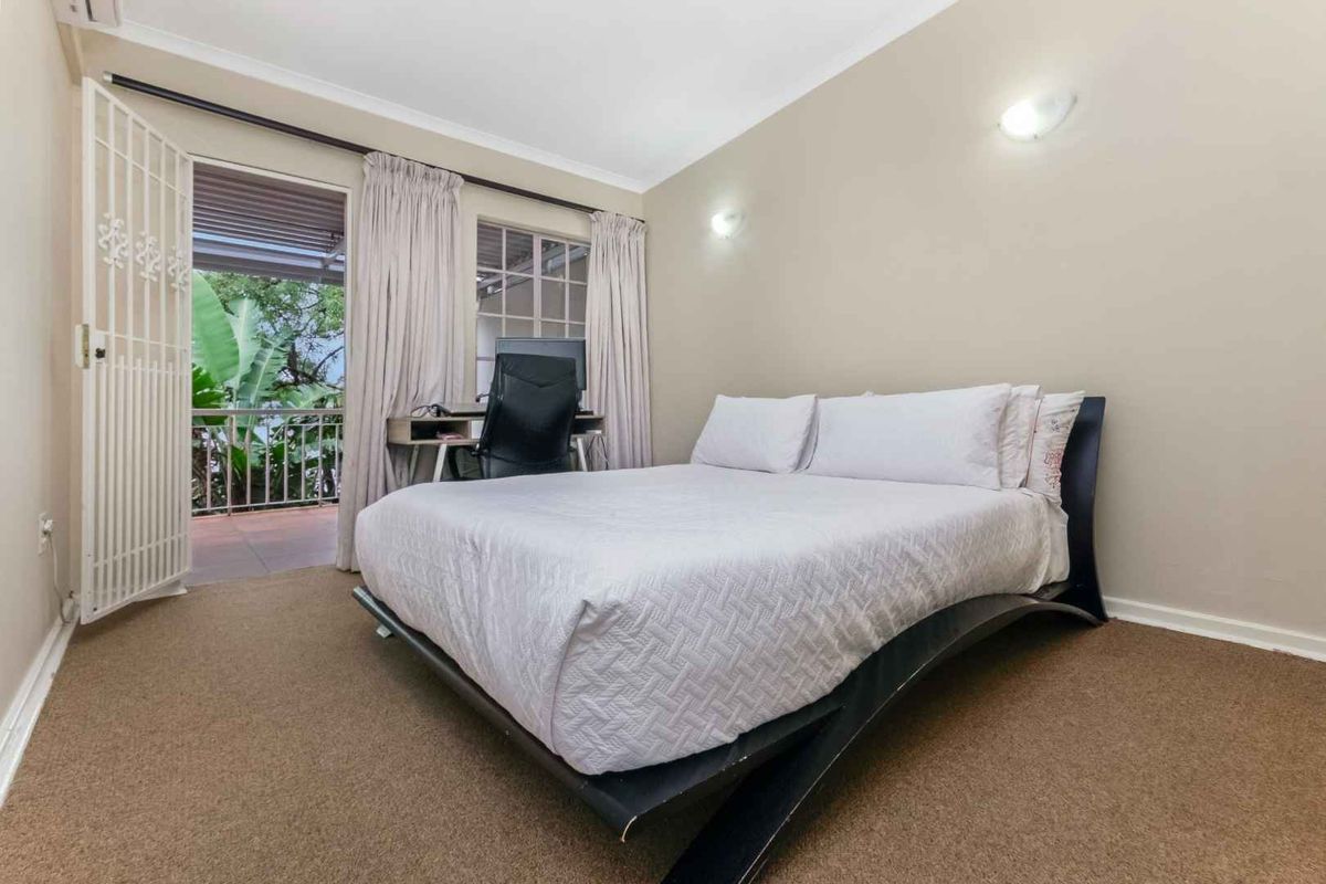 A bedroom featuring carpeted flooring, wall-mounted lighting, and direct access to an outdoor balcony through a security gate.