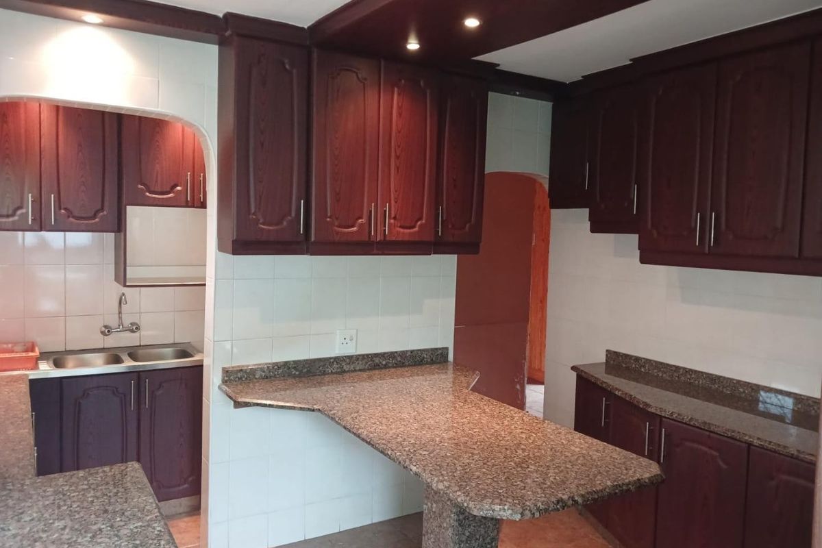A spacious kitchen featuring dark wood cabinetry, granite countertops, a breakfast bar, and a separate scullery area with a double sink.